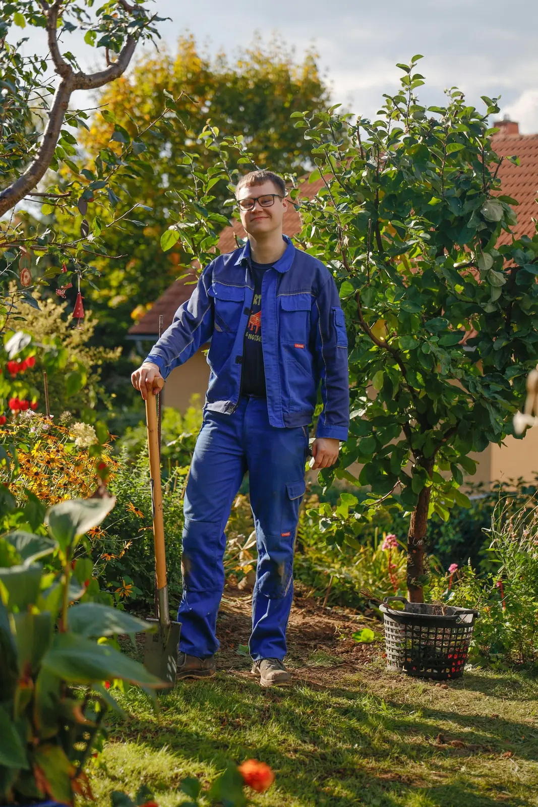 Smiling gardener in blue work clothes leaning on a shovel in a garden